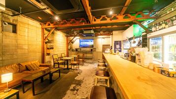 A bar area with a wooden counter, stools, a sofa, and a television screen.