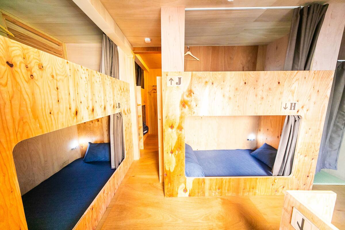 A room with bunk beds made of wood, a small table, and a hanging light fixture.