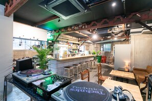A bar area with a DJ setup, bar stools, and a counter with various bottles. - Momodaniagito - Hostel (Osaka)