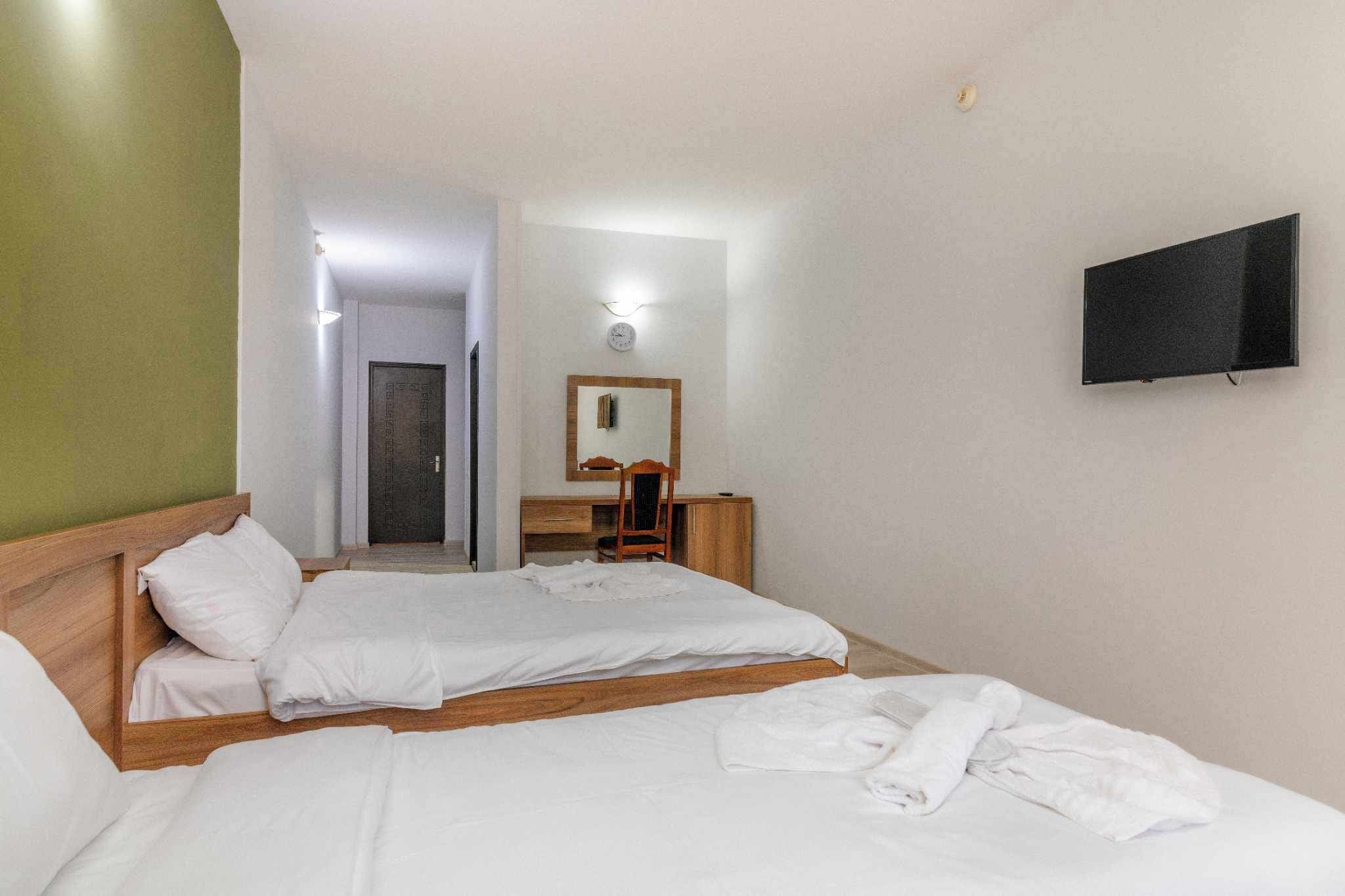 A hotel room with two beds, a desk, a chair, a mirror, and a TV.