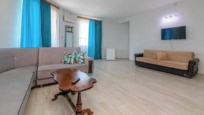 A living room with a sectional sofa, a smaller sofa, a wooden coffee table, and a flat-screen TV mounted on the wall. - Victoria Hotel (Gori)