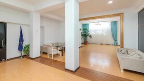 A spacious living area with a sofa, a dining table, and chairs. There is a potted plant and a blue flag with stars. - Victoria Hotel (Gori)