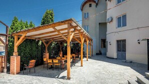 A covered outdoor seating area with tables and chairs, a stone-paved courtyard, and a building with a light-colored facade and windows. - Victoria Hotel (Gori)