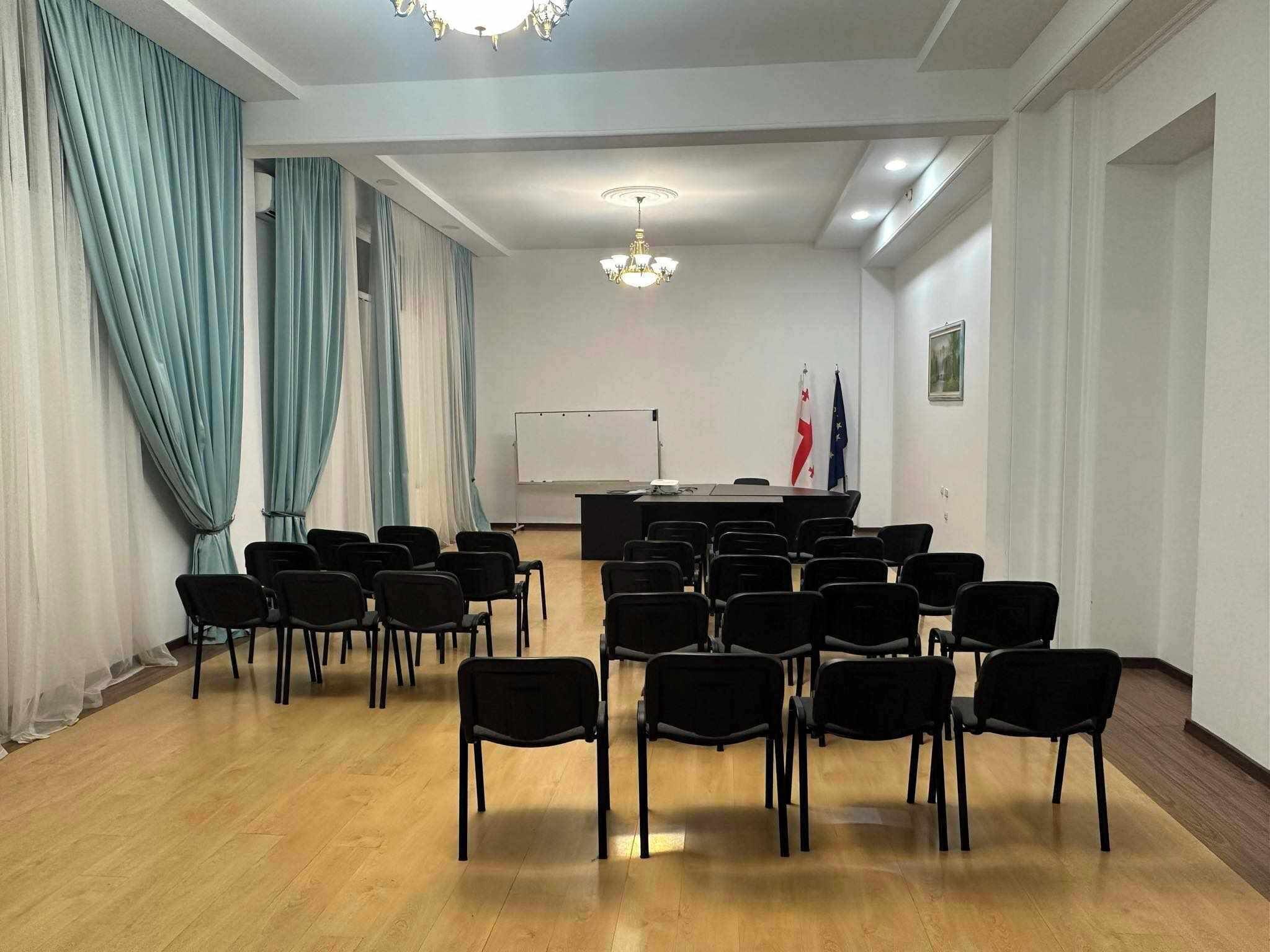 Une salle de conférence équipée d’un tableau blanc, d’une table avec des chaises et de drapeaux accrochés au mur.