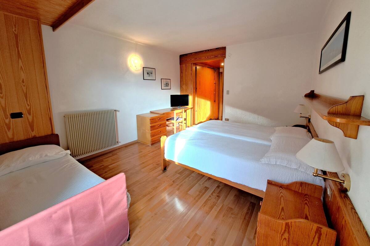 Un dormitorio con dos camas, un escritorio de madera, una silla, un radiador y un televisor.