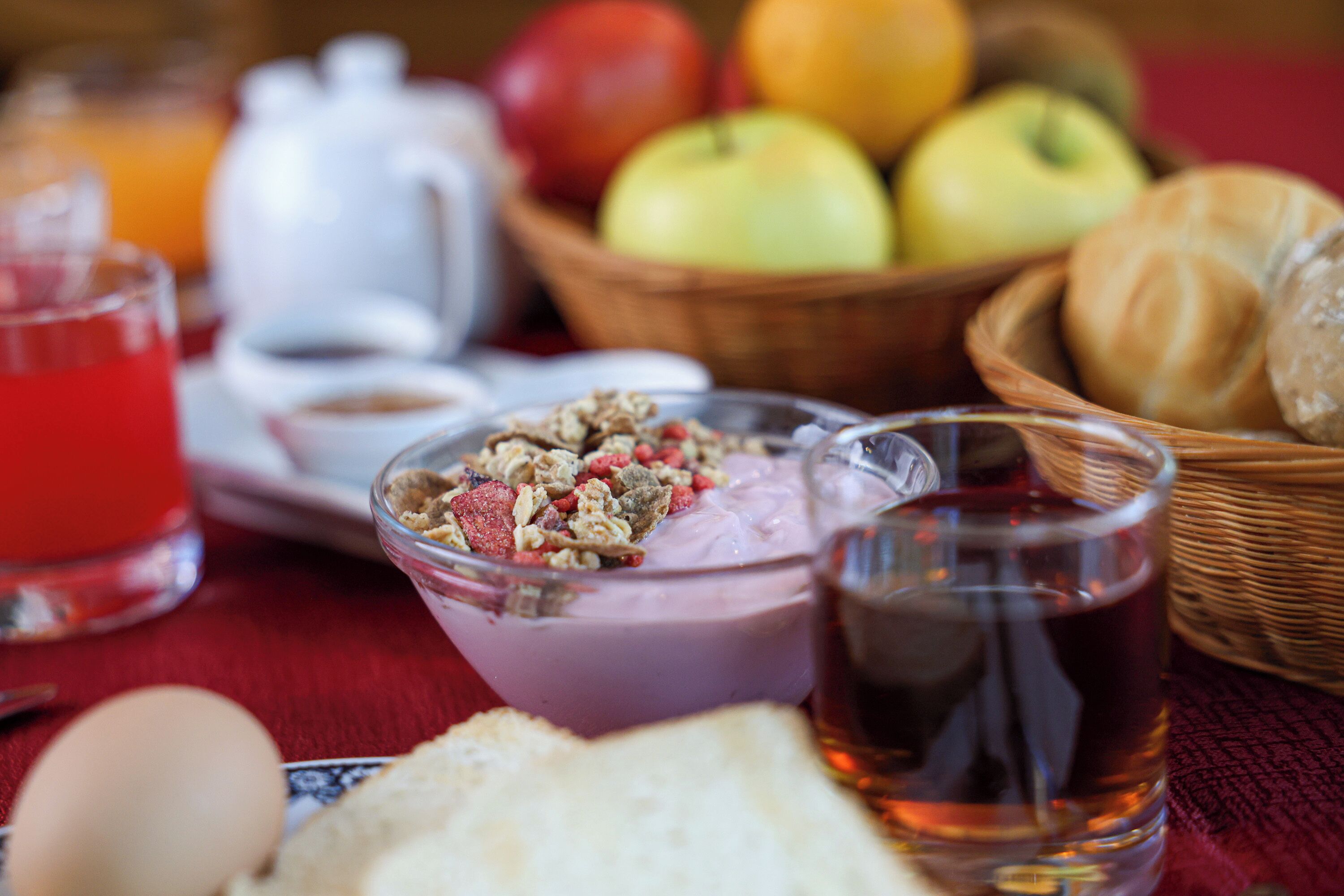 Un desayuno con un tazón de yogur, un vaso de jugo, un croissant y una cesta de frutas.