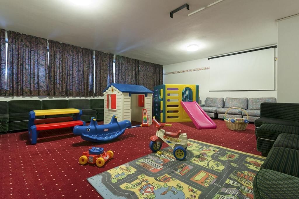 A living room with a red carpet, a blue toy boat, a toy train, and a playhouse.