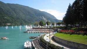 A lakeside view with boats, a dock, and a park area with trees and flowers. - Lake & Nature Hotel Gloria (Molveno)