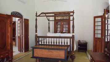 A traditional four-poster bed with a wooden frame and a matching bench in a room with white walls and a patterned carpet.