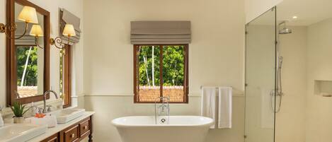 A bathroom with a freestanding bathtub, a glass-enclosed shower, a vanity with a mirror, and a window with a view of trees.