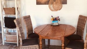 A dining area with a round wooden table, wicker chairs, a hanging rattan light, and a wall-mounted painting.