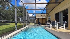Ein Schwimmbad mit überdachtem Bereich, eine Terrasse mit Liegestühlen und im Hintergrund ein Haus.