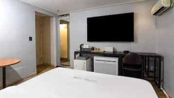 Een hotelkamer met een bed, een bureau, een stoel, een airconditioner en een aan de muur bevestigde televisie.