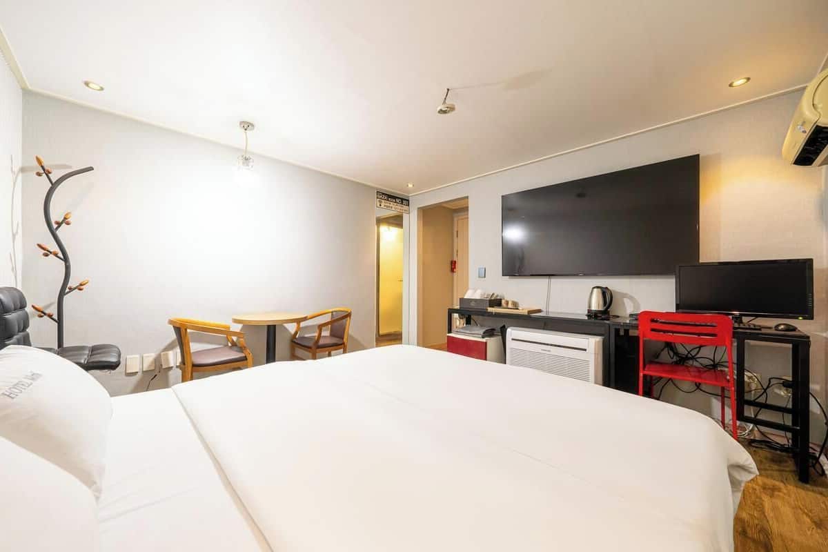 Une chambre d’hôtel avec un grand lit, un bureau avec un ordinateur, une télévision et une chaise.