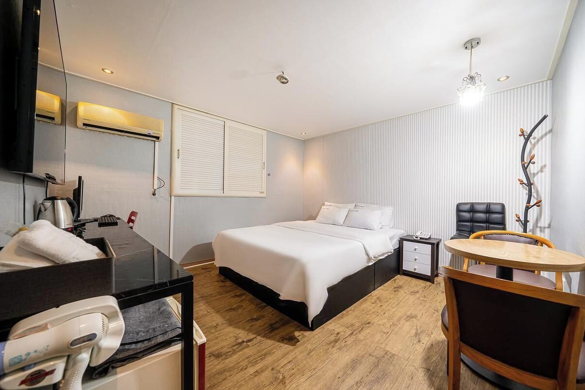 Une chambre d’hôtel comprenant un lit, une table de chevet, une chaise et un bureau avec un miroir et un sèche-cheveux.