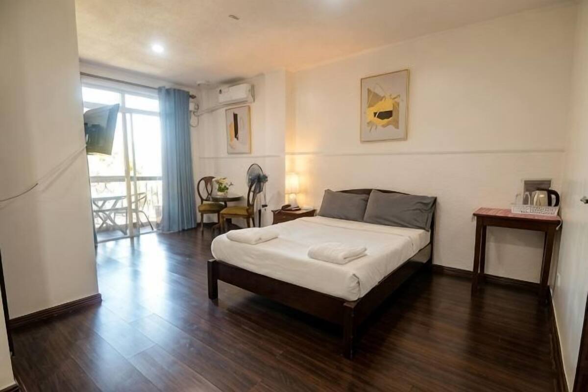 A hotel room with a bed, a desk, a chair, a small table, and a balcony.