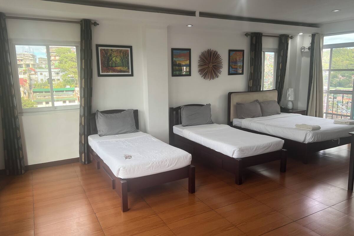 A hotel room with two single beds, a large window with curtains, and artwork on the walls.