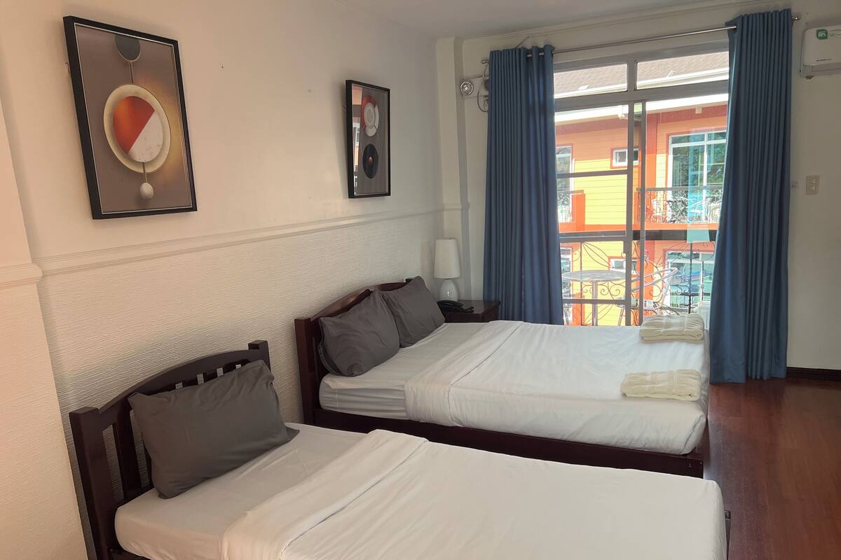 A hotel room with two beds, a window with blue curtains, and a view of an outdoor area.