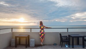 Una donna in piedi su un balcone con vista sul mare al tramonto.