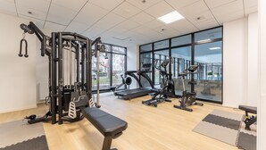 Een fitnessruimte met een bank, diverse fitnessapparaten en grote ramen met uitzicht op buiten.