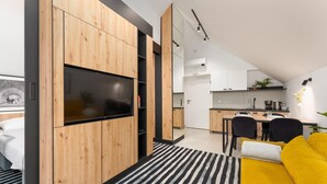 Een moderne woonkamer met een televisie, houten kasten, een gele bank en een gestreept vloerkleed.