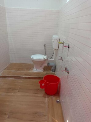 Une petite salle de bain avec des toilettes, un seau rouge et un espace douche.