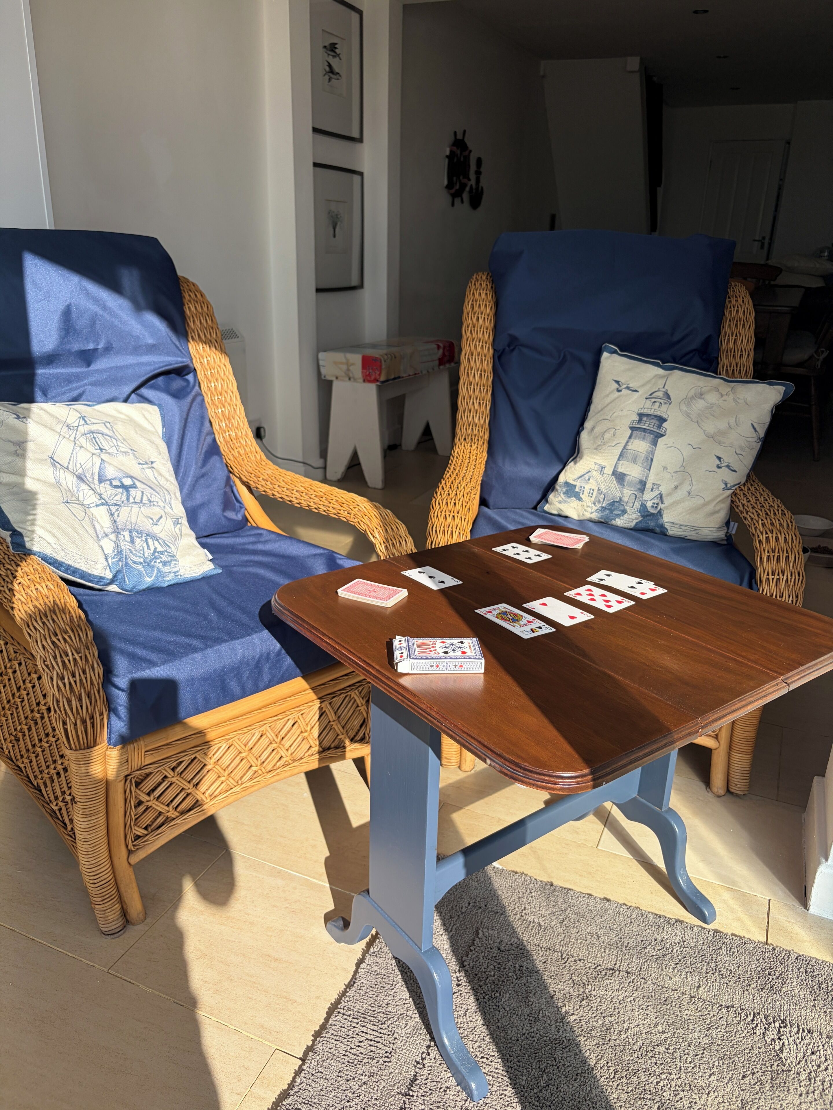 Two wicker chairs with blue cushions and a wooden table with playing cards.