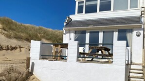 A white building with large windows, a balcony, and a sandy beach in the background.