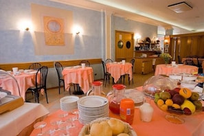 A dining area with tables set for breakfast, including plates, glasses, and a fruit bowl. - Albergo Ristorante Grigna (Mandello del Lario)