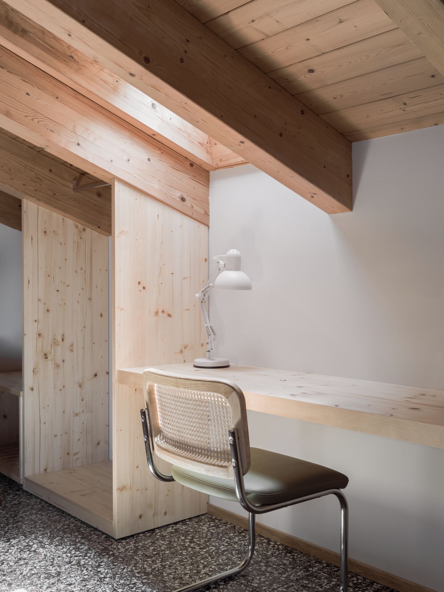 Un espacio de trabajo moderno con un escritorio de madera, una lámpara de escritorio blanca y una silla de metal.