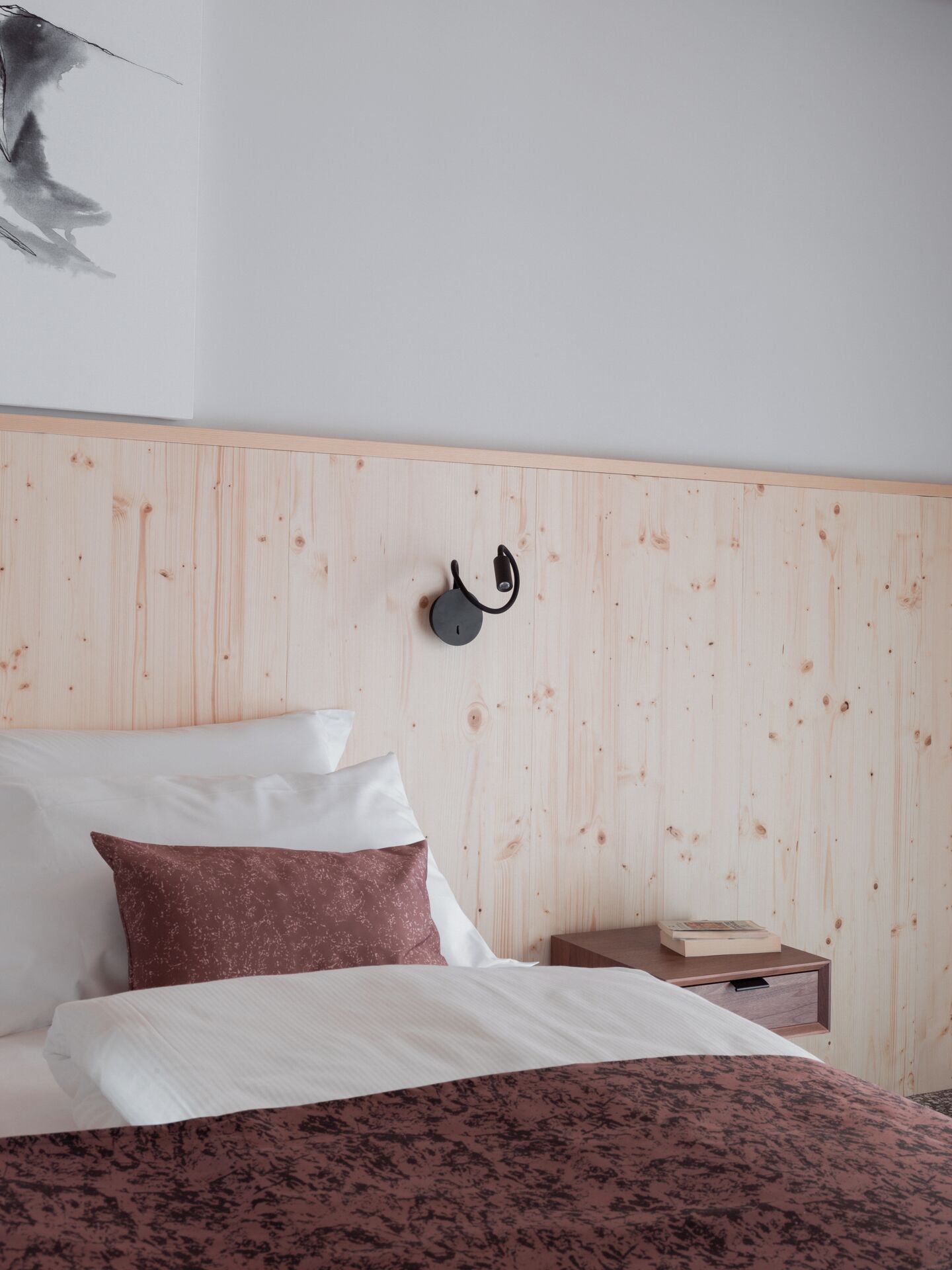 A bedroom with a wooden headboard, a bed with white and brown bedding, a nightstand with a book, and a wall-mounted lamp.