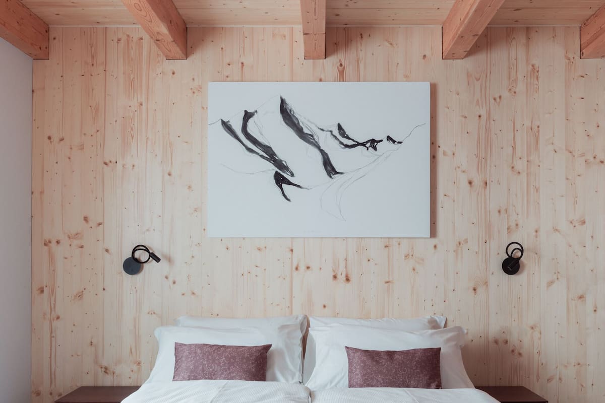 Ein Schlafzimmer mit Holzbalkendecke, einem Bett mit weißer und rosa Bettwäsche und einem schwarzen, abstrakten Gemälde an der Wand.