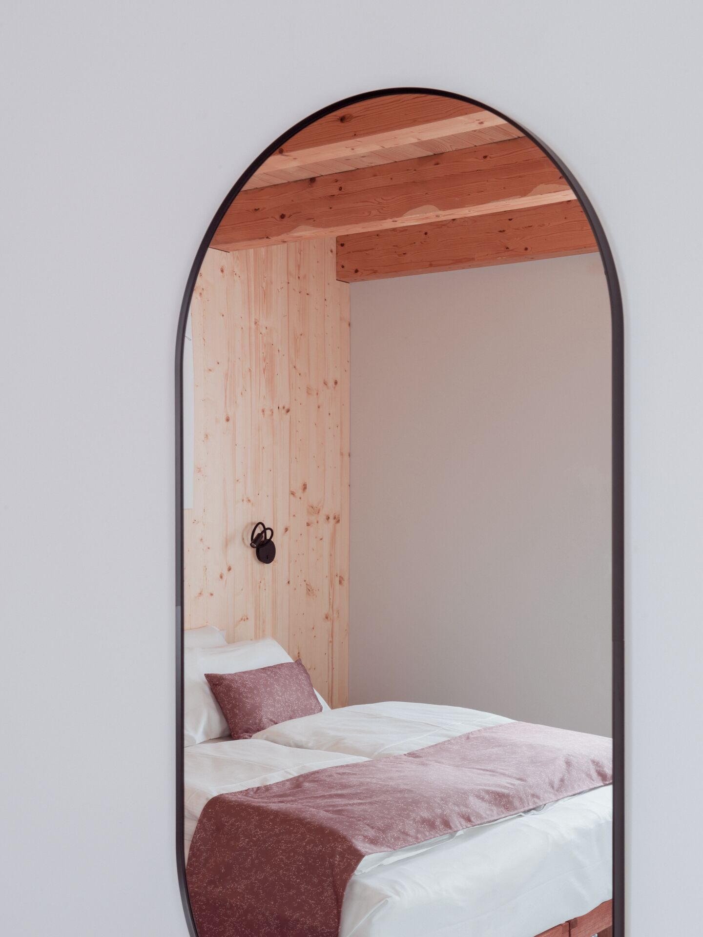 Une chambre avec un plafond en bois, un lit avec une literie blanche et rose, et un luminaire fixé au mur.