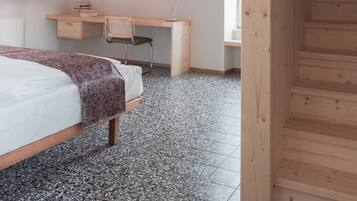 A bedroom with a bed, a desk, and a chair. There is a staircase leading to an upper level.
