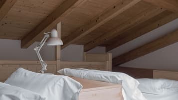 A bedroom with a sloped ceiling, wooden beams, a single bed with white bedding, and a desk lamp.