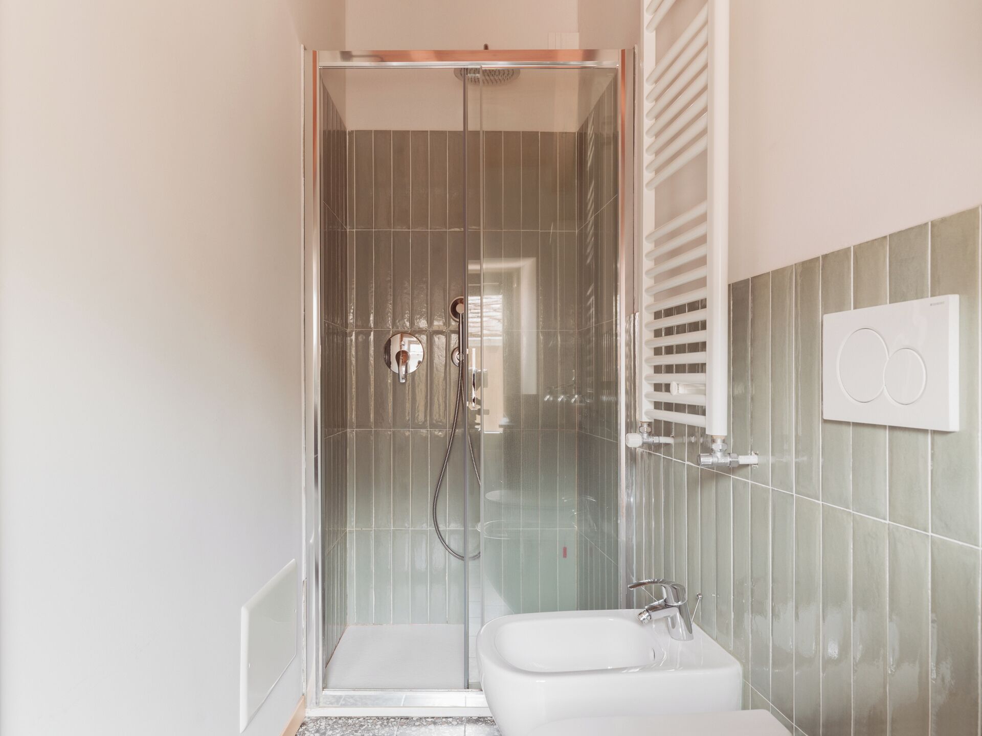 Un bany modern amb dutxa amb envà, un lavabo blanc i un suport per a tovalloles.