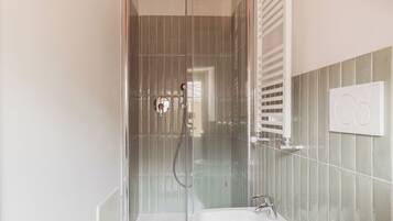 Un bany modern amb dutxa amb envà, un lavabo blanc i un suport per a tovalloles.
