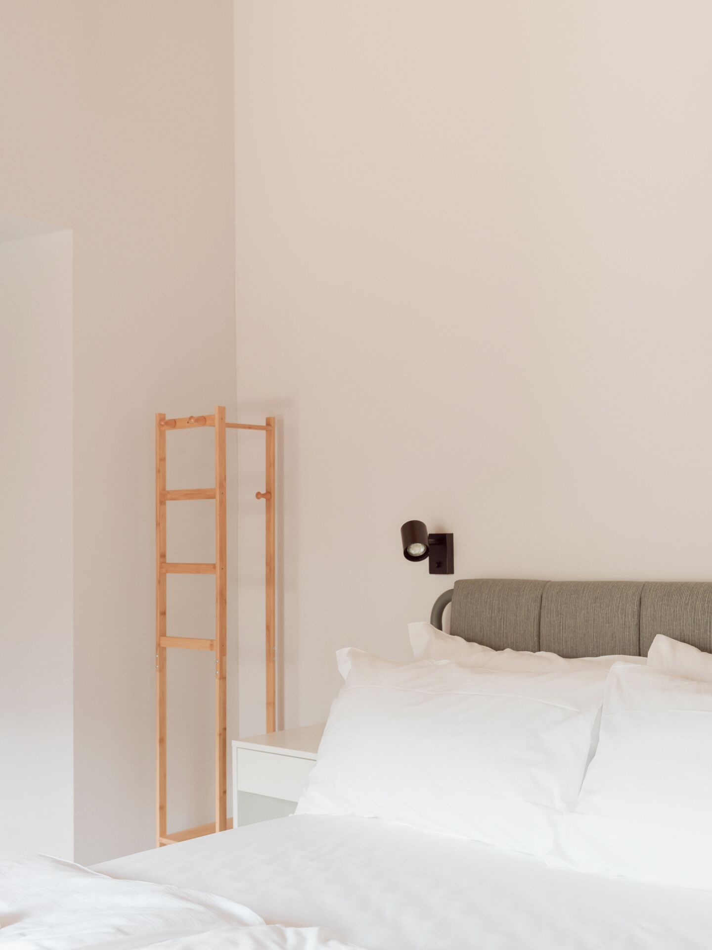 A bedroom with a bed, white bedding, a wooden ladder, and a wall-mounted light fixture.