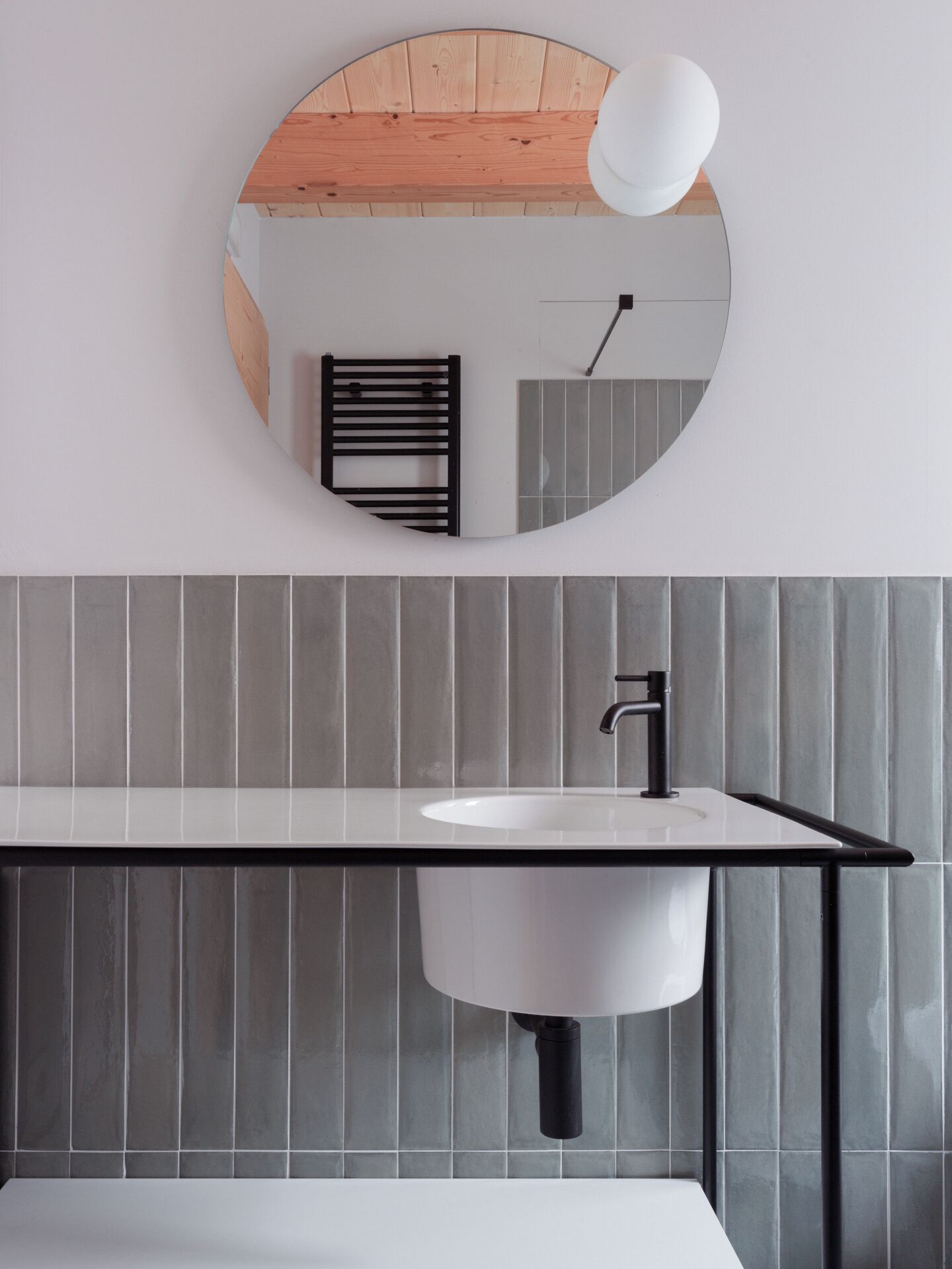 Un baño moderno con un espejo redondo, un lavabo blanco y un techo de madera.
