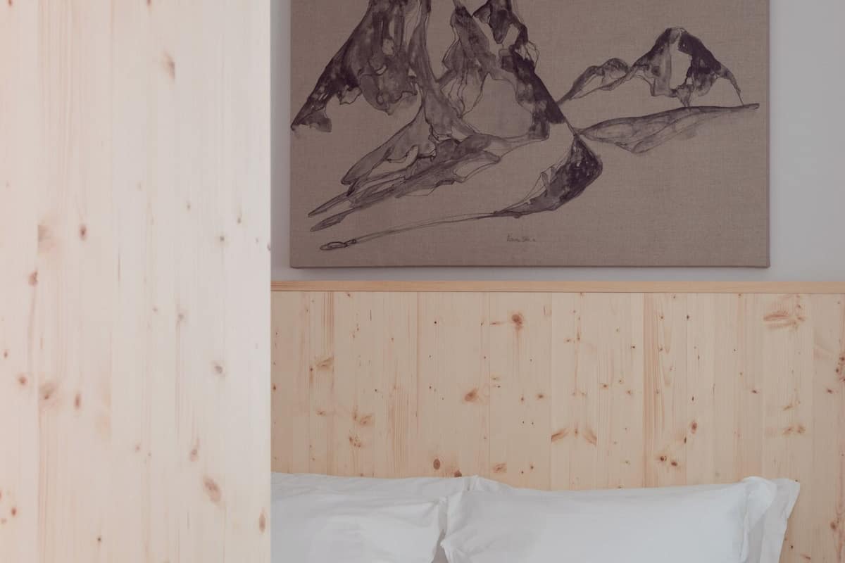 Ein Schlafzimmer mit einem Holz-Kopfteil, einem Bett mit weißen Bettwäsche und einem Gemälde von Bergen an der Wand.