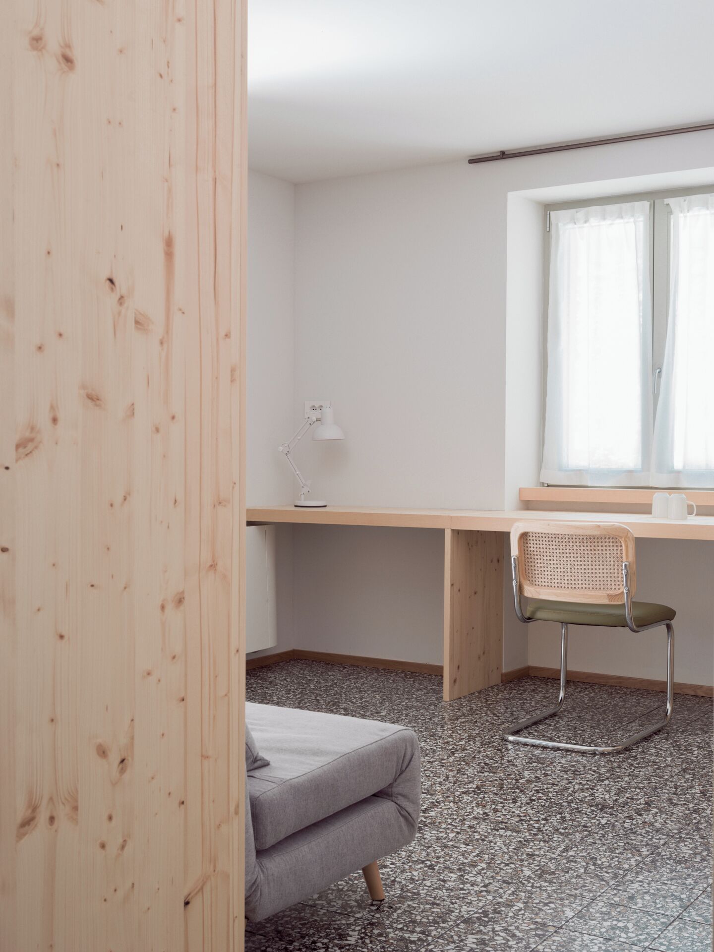 Een strak ingerichte kamer met een houten bureau, een stoel, een lamp en een raam met gordijnen.