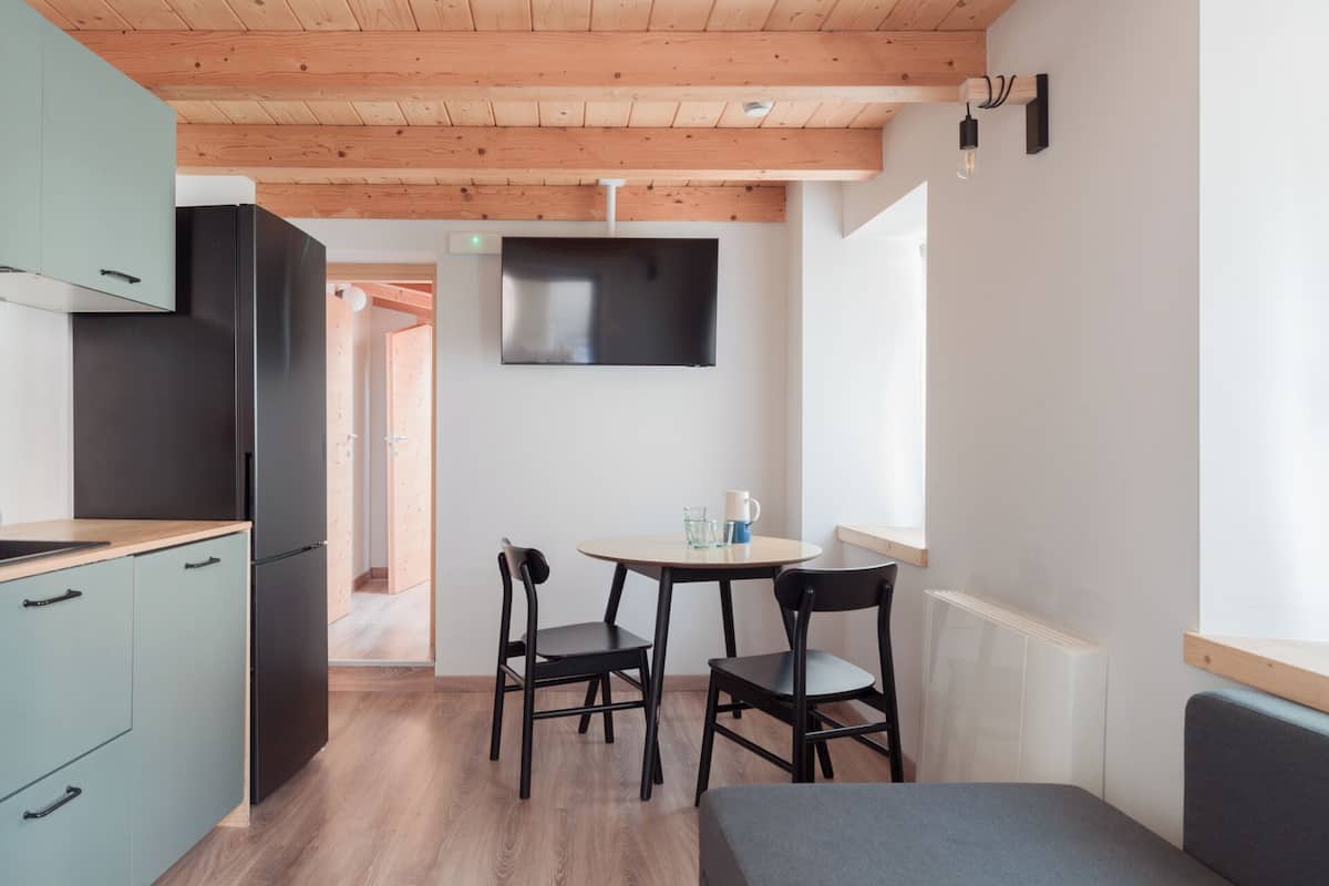 Eine moderne Küche mit Holzbalkendecke, einem schwarzen Kühlschrank und einem Essbereich mit zwei Stühlen und einem Tisch.