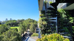 A modern building with a spiral staircase, surrounded by lush greenery and a view of a cityscape in the background. - Penthouse perfection with private rooftop pool paradise. 2 bed, 2 bath, parking (Waterloo)