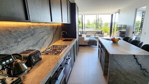 A modern kitchen with a marble countertop, a gas stove, a coffee machine, and a dining area with a marble table and chairs. - Penthouse perfection with private rooftop pool paradise. 2 bed, 2 bath, parking (Waterloo)