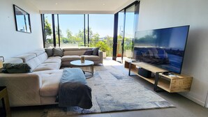 A modern living room with a sectional sofa, a round coffee table, a flat-screen TV, and a balcony with a city view. - Penthouse perfection with private rooftop pool paradise. 2 bed, 2 bath, parking (Waterloo)
