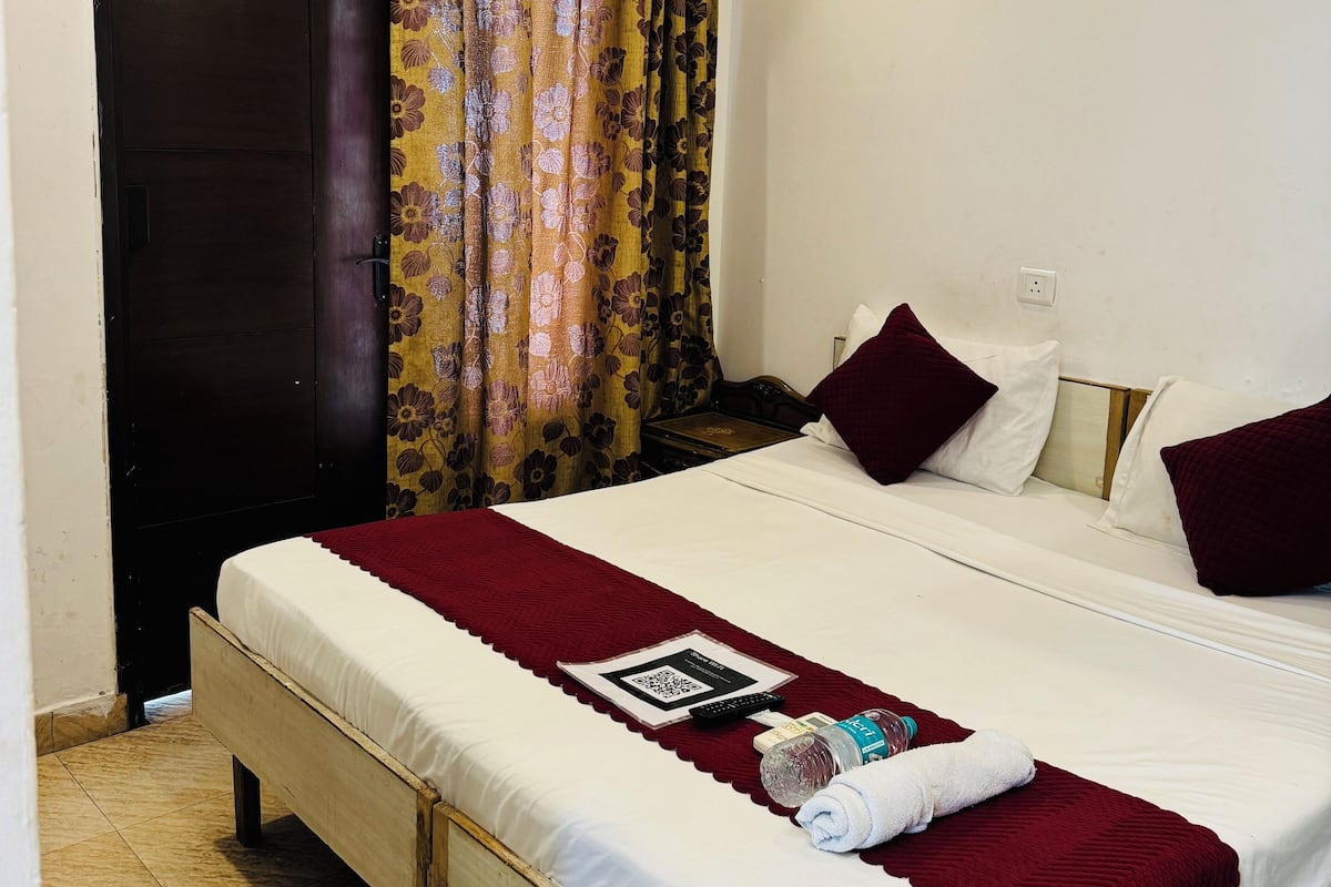 A bedroom with a bed, a window with curtains, an air conditioning unit, and a door.