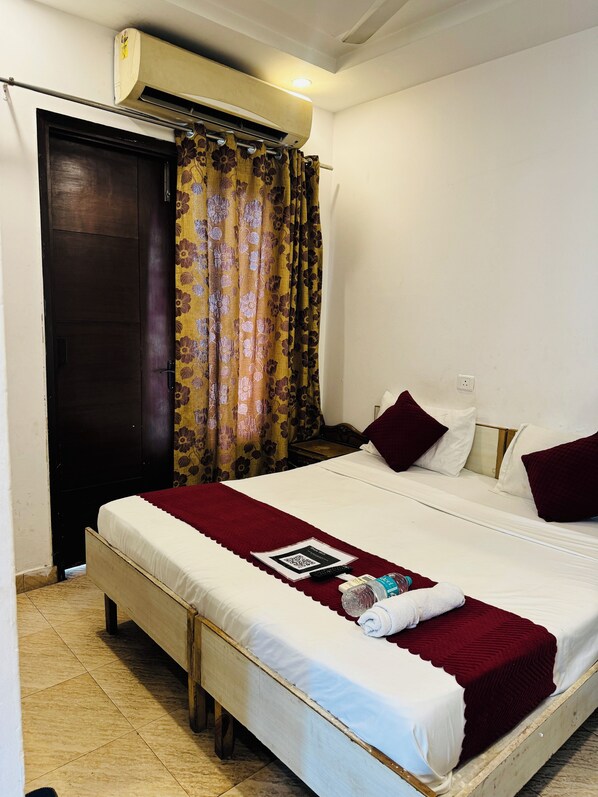 A bedroom with a bed, a window with curtains, an air conditioning unit, and a door. - Bir Home Stays (New Delhi)