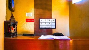 En receptionsdisk med träinredning, en väggmonterad tv, en klocka och en tavla med rumsnummer.