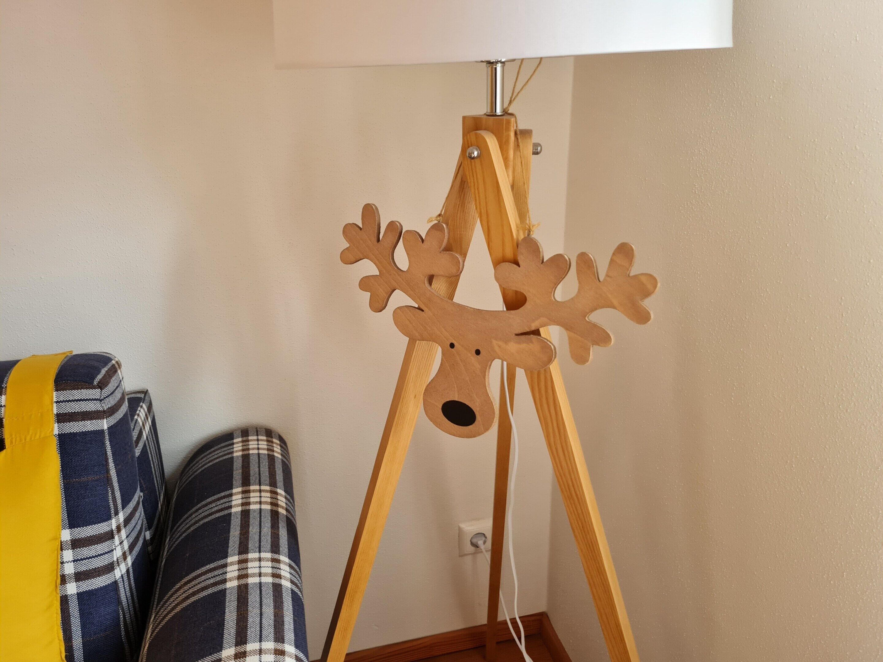 Una escultura de ciervo de madera sobre un atril trípode en una habitación con pared blanca y sofá a cuadros.