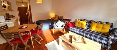 A compact living space with a kitchenette, a dining area, a sofa, and a small wooden table.